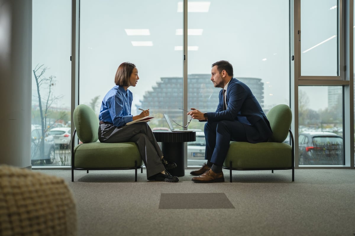 Two professionals in a modern office in a focused planning conversation, one taking notes