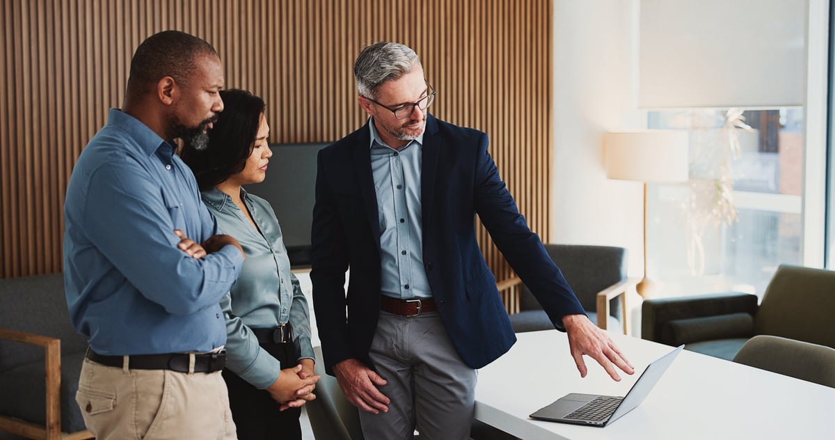 A business team in an office reviewing plans and giving feedback around a laptop