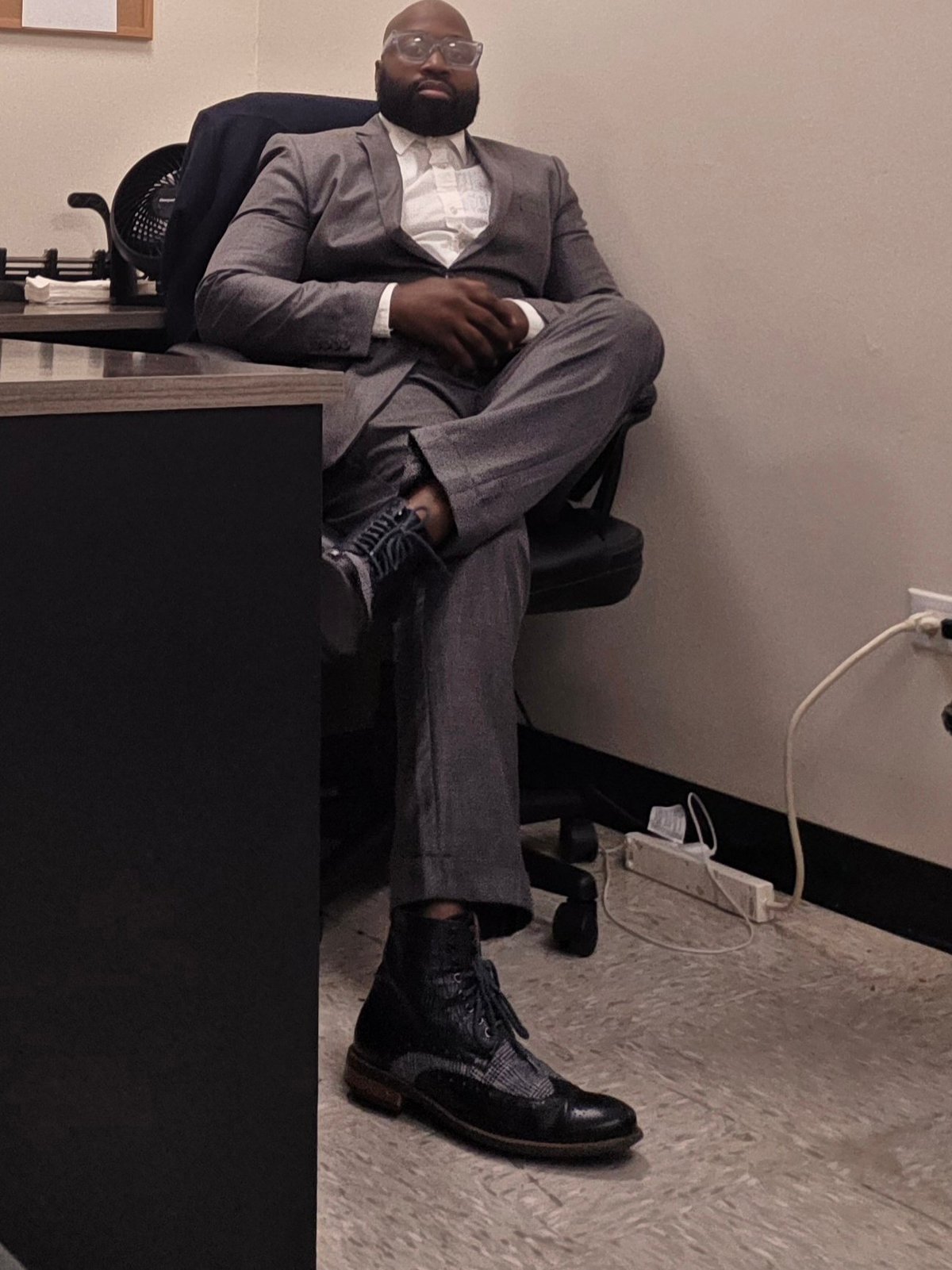Justice Cephas, owner and operator of Kapital Enterprises, seated at a desk in a grey suit and glasses