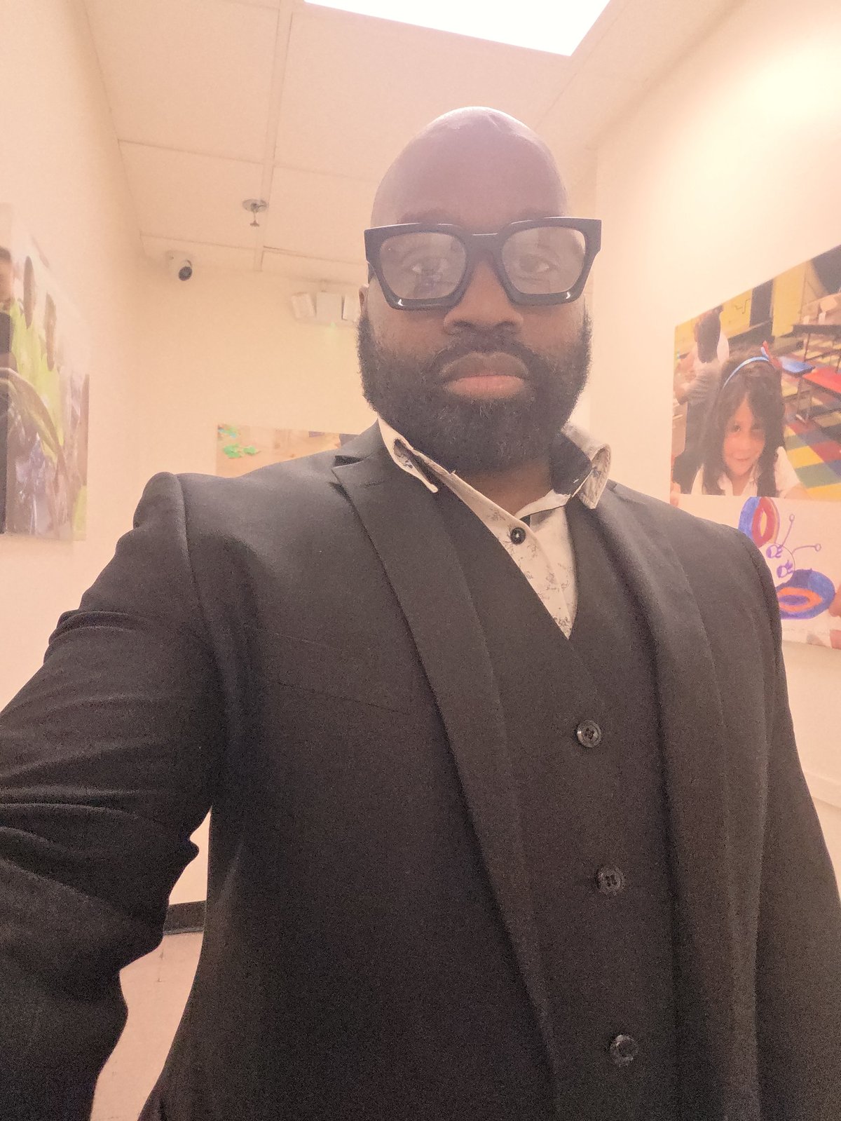 Justice Cephas, owner and operator of Kapital Enterprises, wearing a dark blazer and glasses in an art gallery with colourful artwork behind him